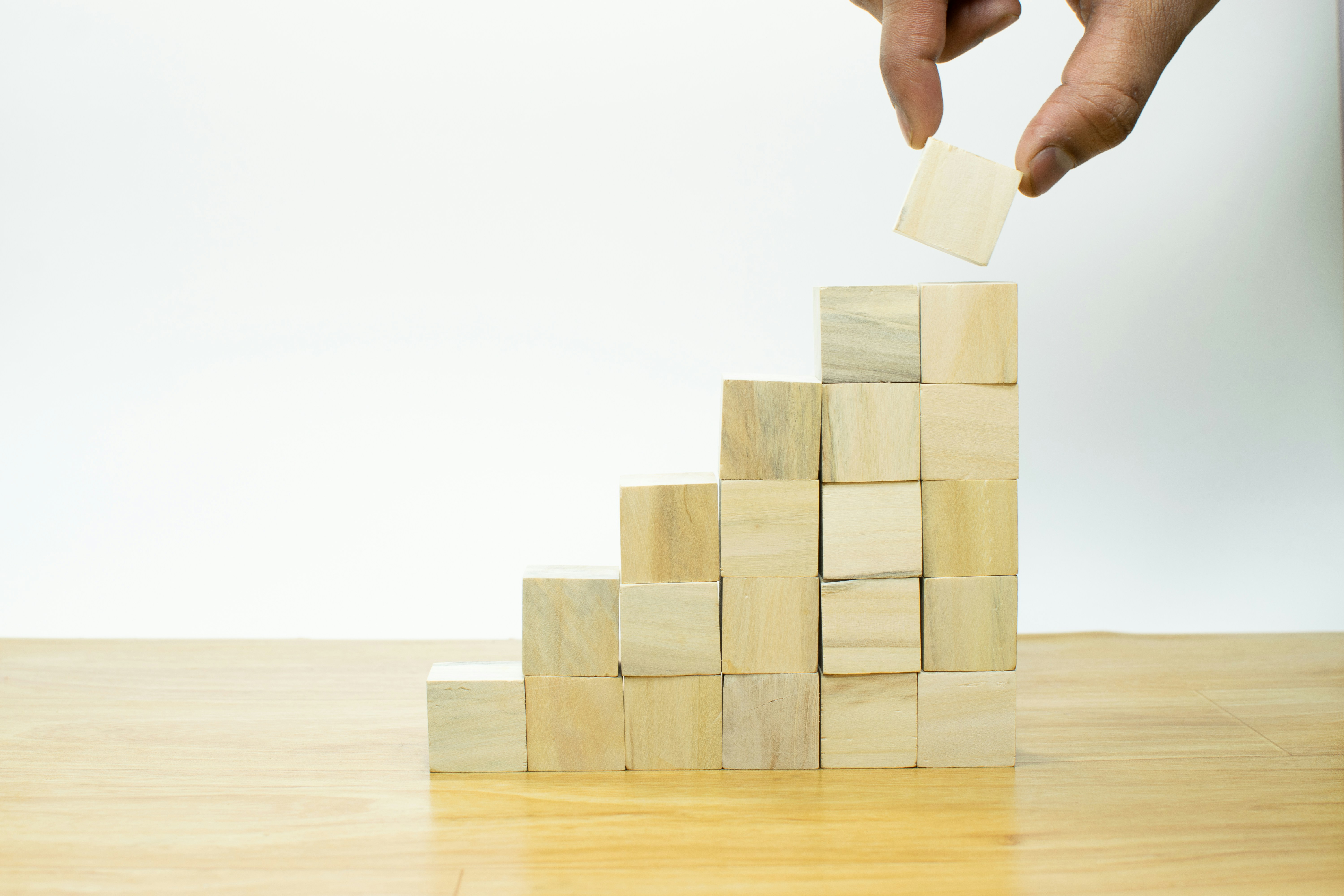 A hand placing a wooden block on top of a rising staircase of blocks